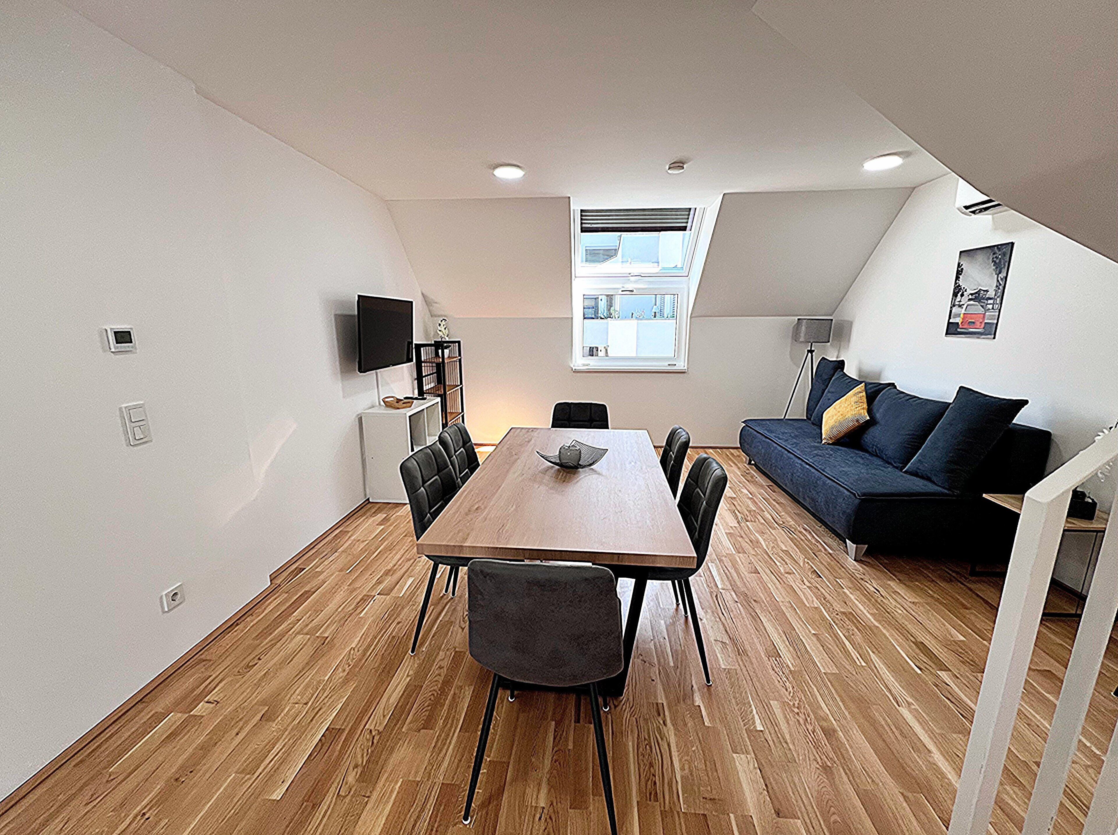 A modern, compact living space with a dining area, a sofa, and a TV mounted on the wall.