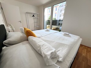 A hotel room with two beds, a window with a view of buildings, a metal drying rack, and a lamp. - Apartments next to Public Transport GG13 (Vienna)