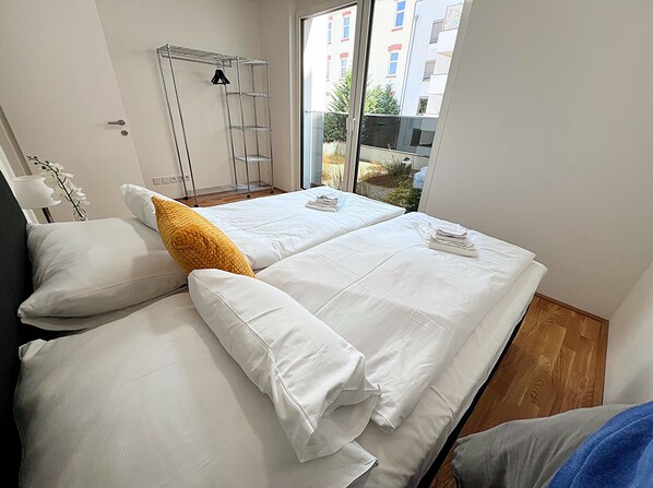 A hotel room with two beds, a metal drying rack, and a view of buildings and greenery outside. - Apartments next to Public Transport GG13 (Vienna)