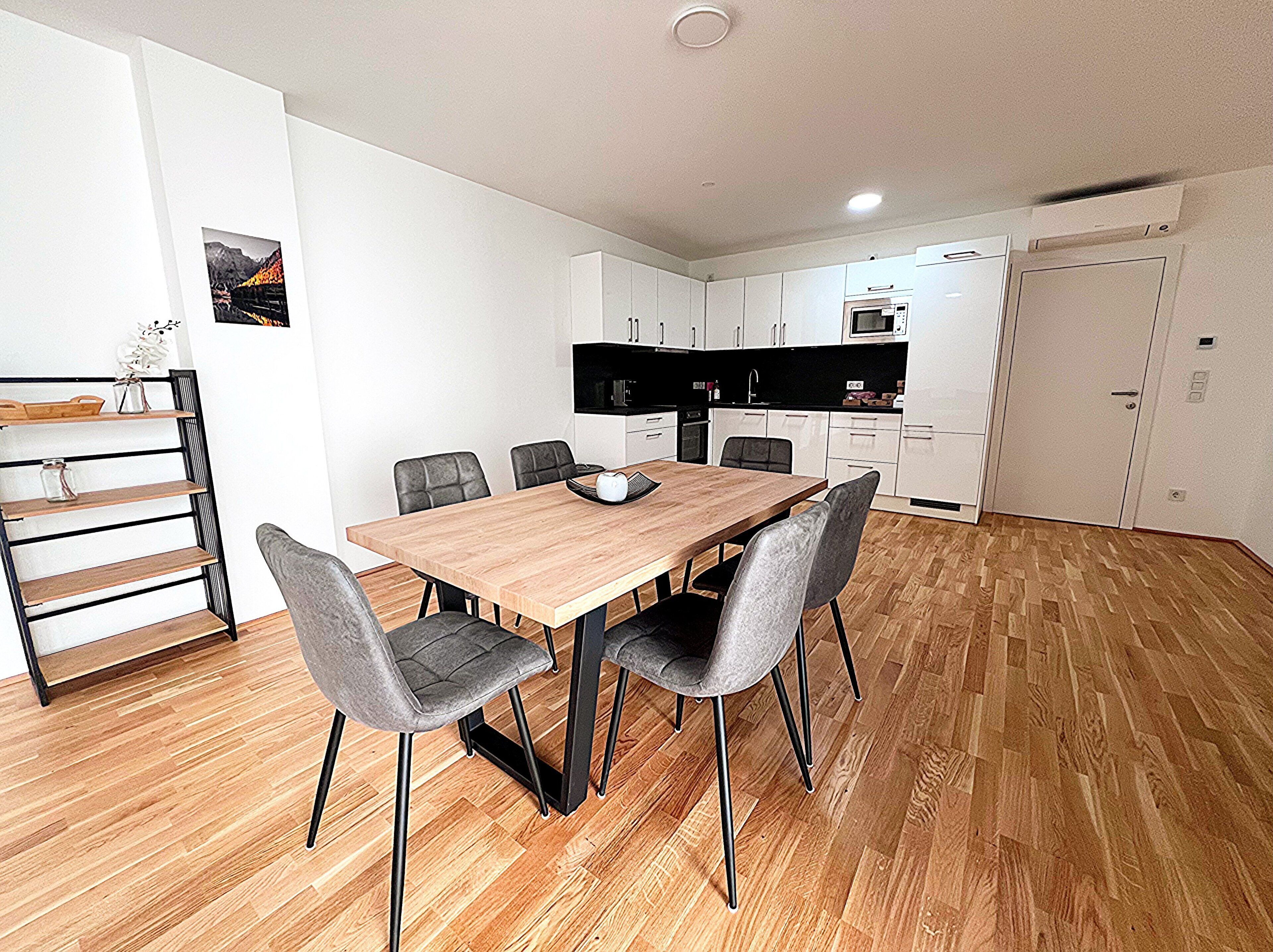 A modern kitchen with white cabinets, a wooden dining table, and grey chairs.