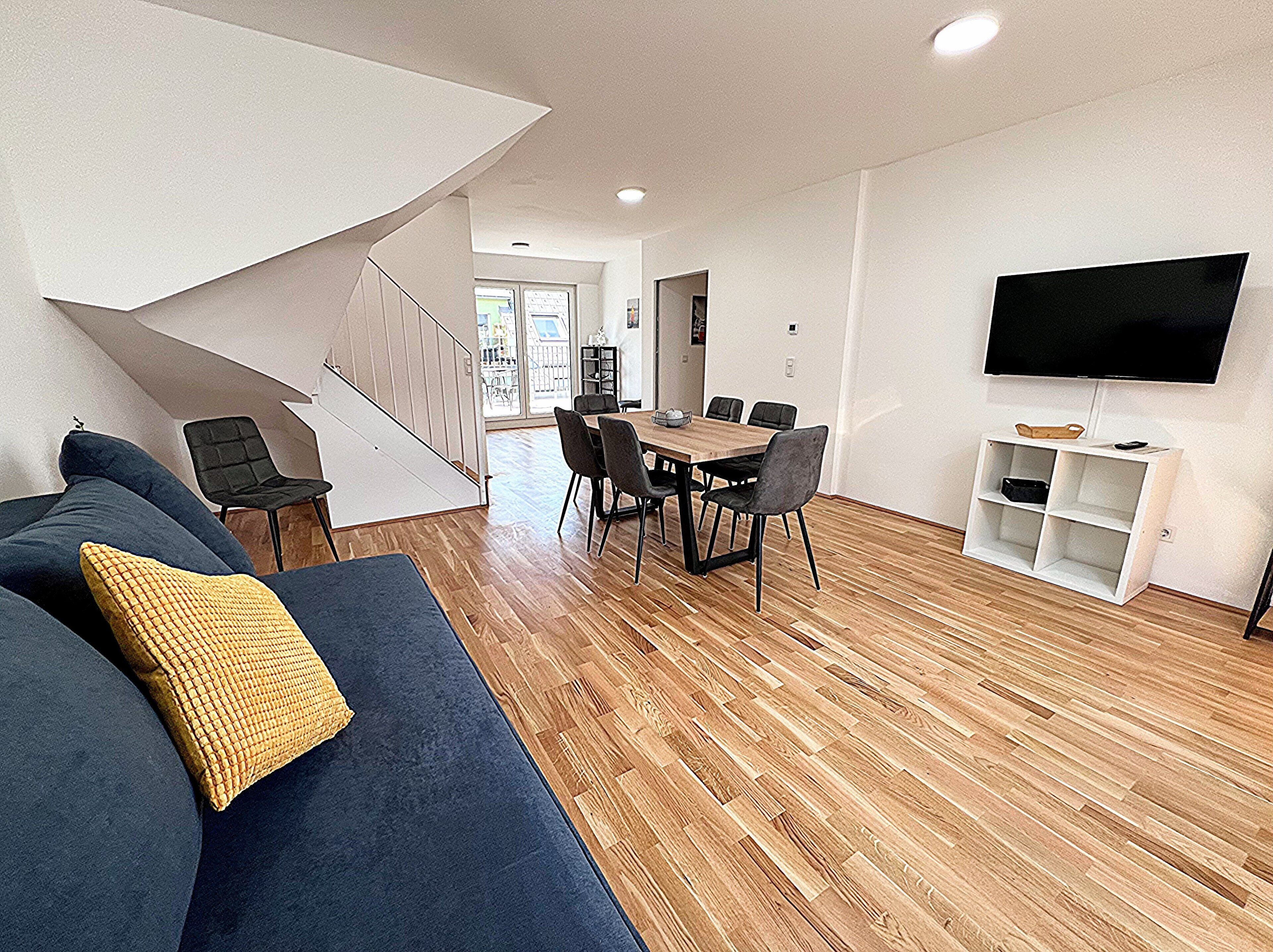 Una sala de estar moderna con sofá, mesa de comedor, sillas, televisor y una escalera.