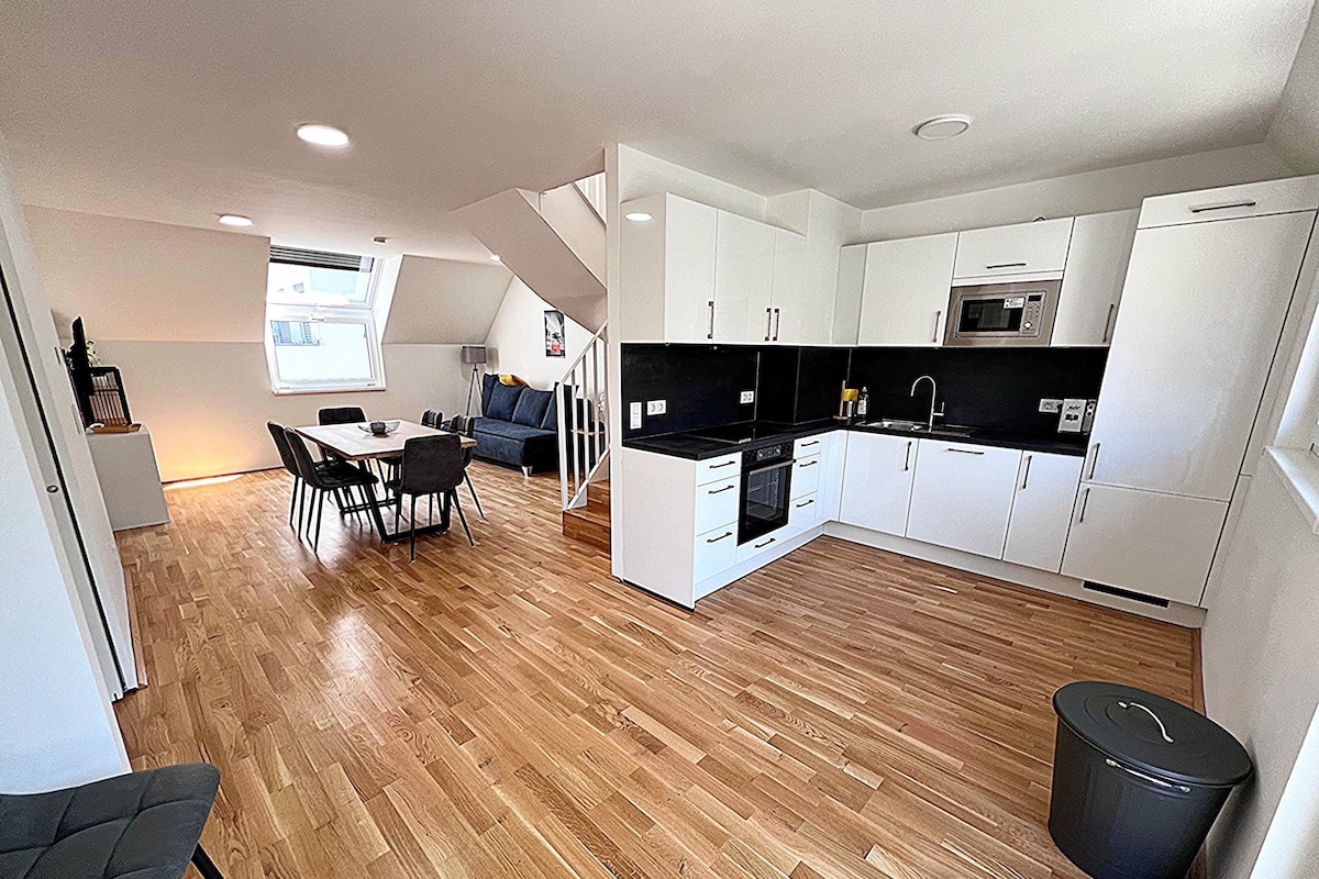 A modern kitchen with white cabinets, a black countertop, and a wooden floor.