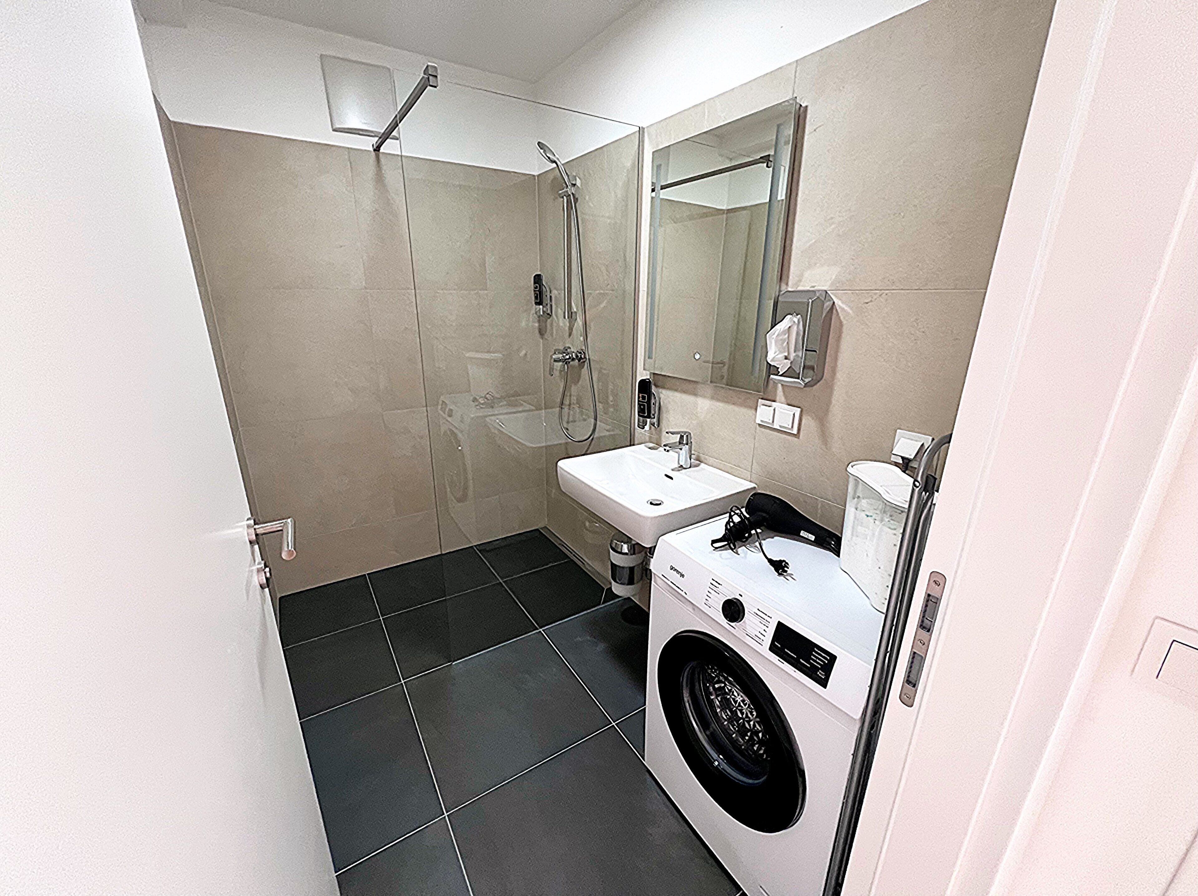 A compact bathroom with a shower, sink, and built-in washing machine.