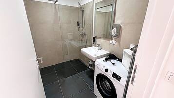 A compact bathroom with a shower, sink, and built-in washing machine.