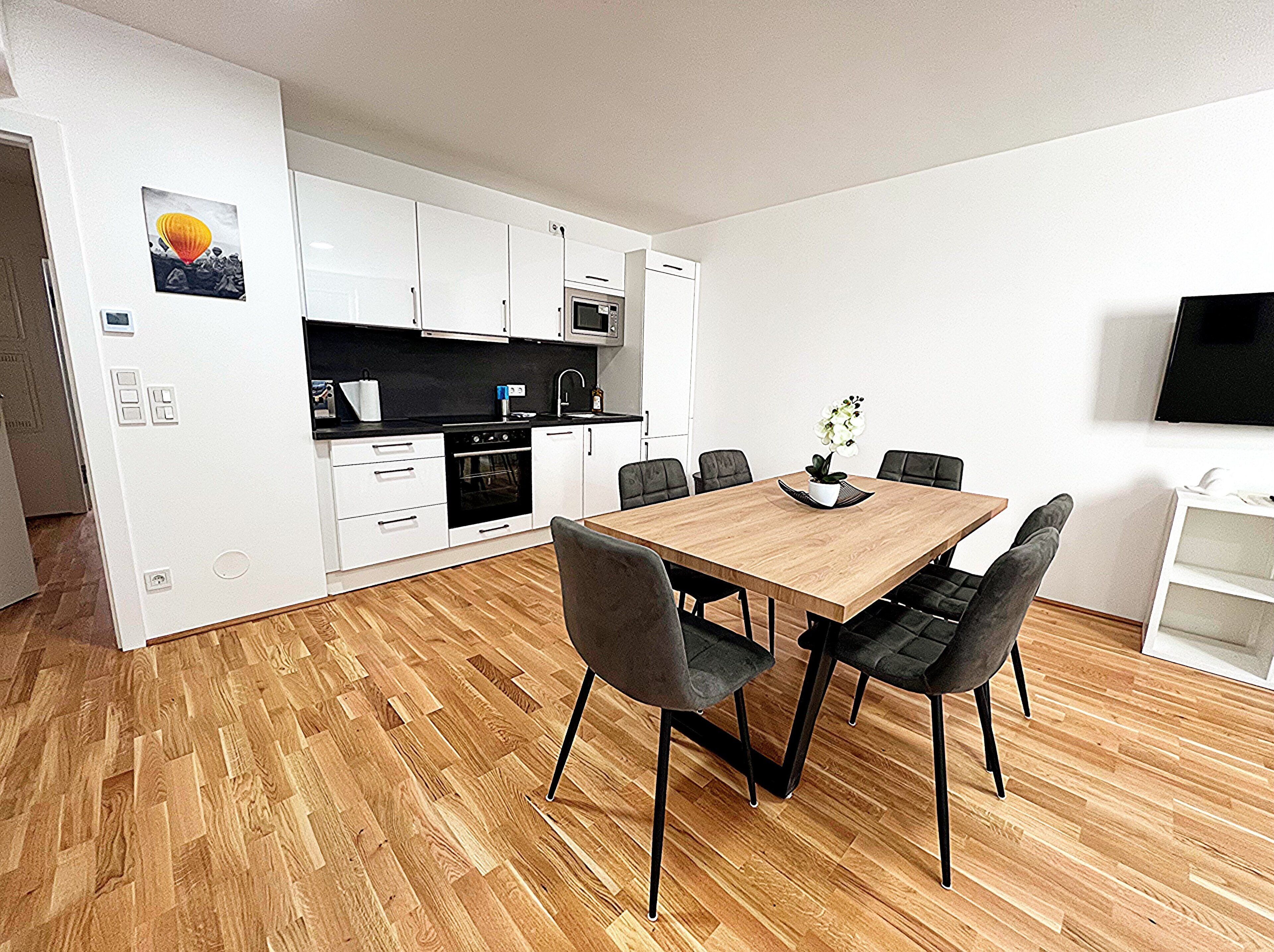 A modern kitchen with white cabinets, a wooden dining table, and black chairs.