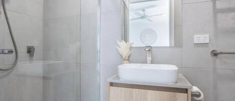 A modern bathroom with a glass shower enclosure, a white sink with a wooden cabinet, and a ceiling fan.