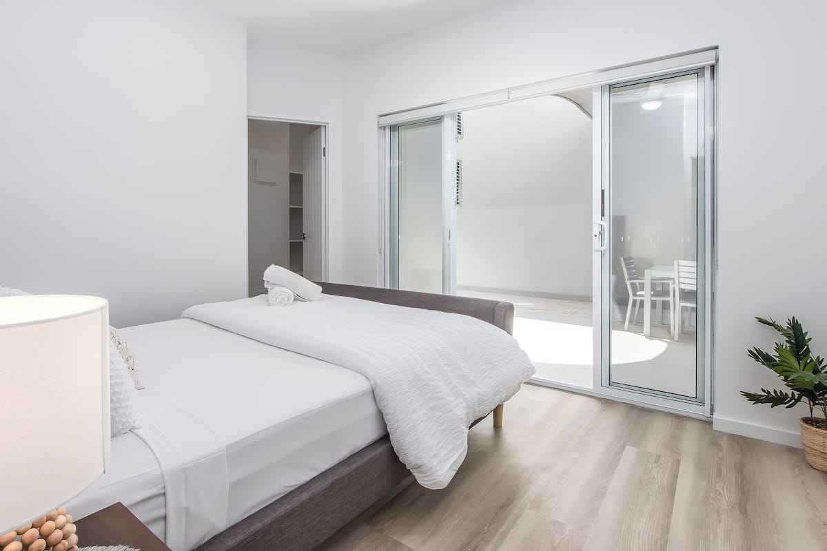 Een moderne slaapkamer met een bed, nachtkastje, kledingkast en een schuifglazen deur naar een balkon.