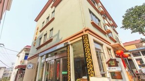 Un edificio de varios pisos con fachada color beige y detalles en rojo. Hay un escaparate con puertas de vidrio y un letrero encima.