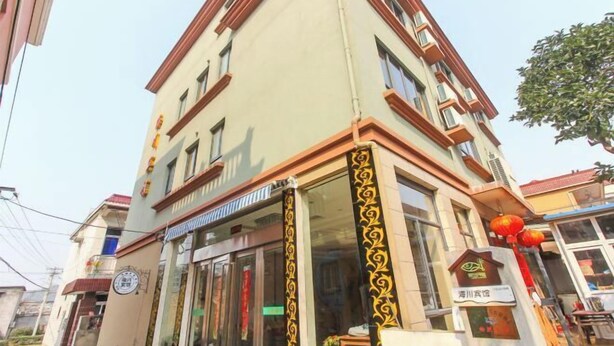 A multi-story building with a beige facade and red trim. There is a storefront with glass doors and a sign above it. - Shengsi Haichuan Hotel (Shengsi)