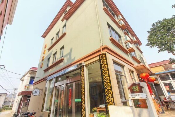 A multi-story building with a beige facade and red trim. There is a storefront with glass doors and a sign above it. - Shengsi Haichuan Hotel (Shengsi)