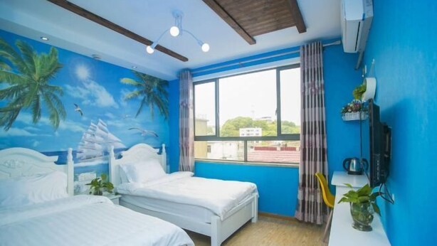 Una habitación con dos camas, un ventanal grande y un mural con palmeras y un velero.