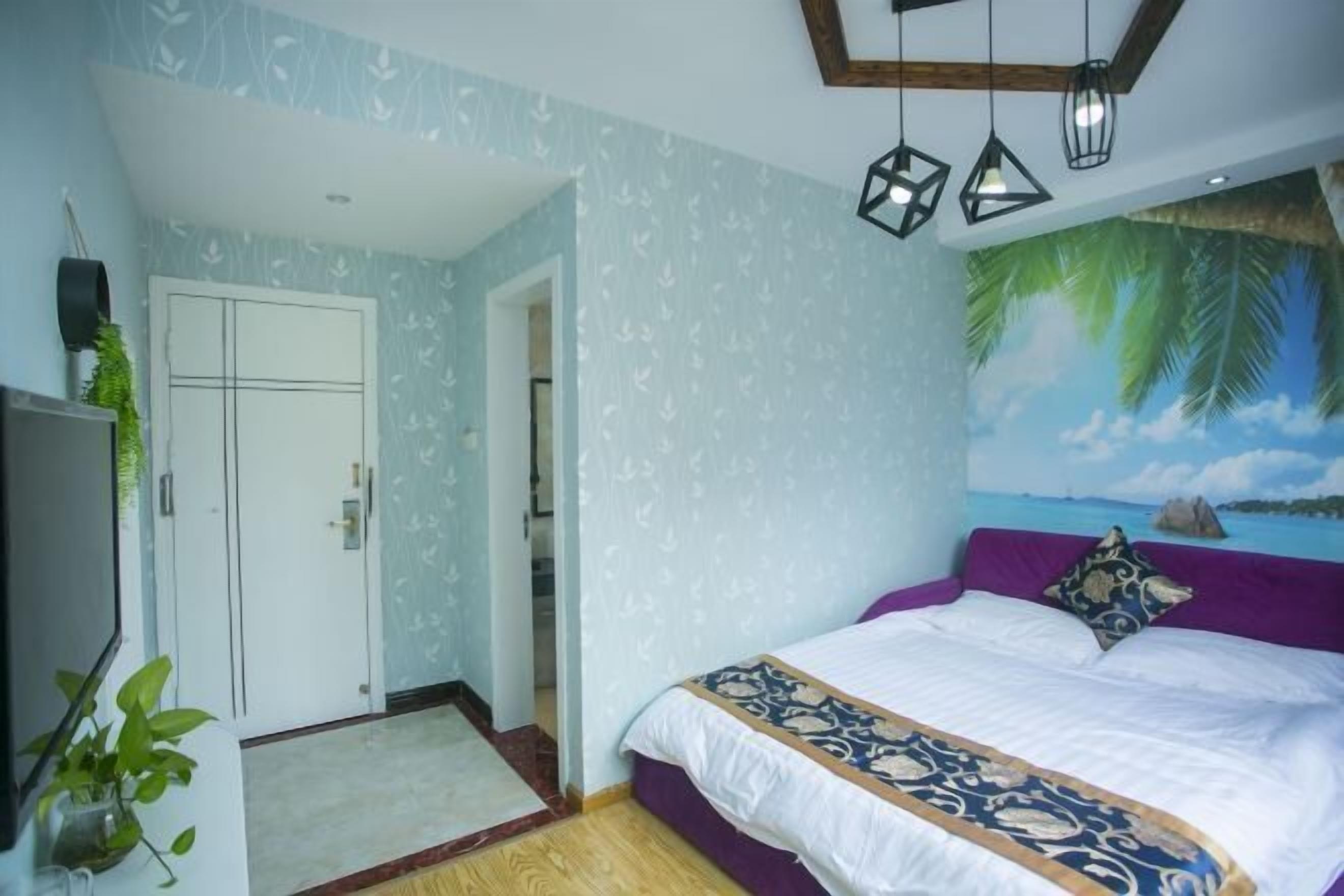 A bedroom with a bed, a door, a wall with a tropical mural, and hanging pendant lights.