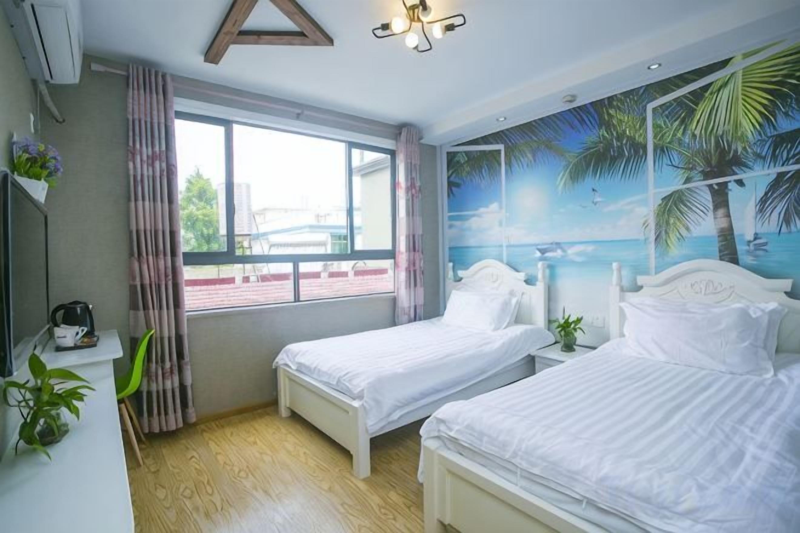 A bedroom with two beds, a window with curtains, a wall mural, and a small bedside table with a plant.