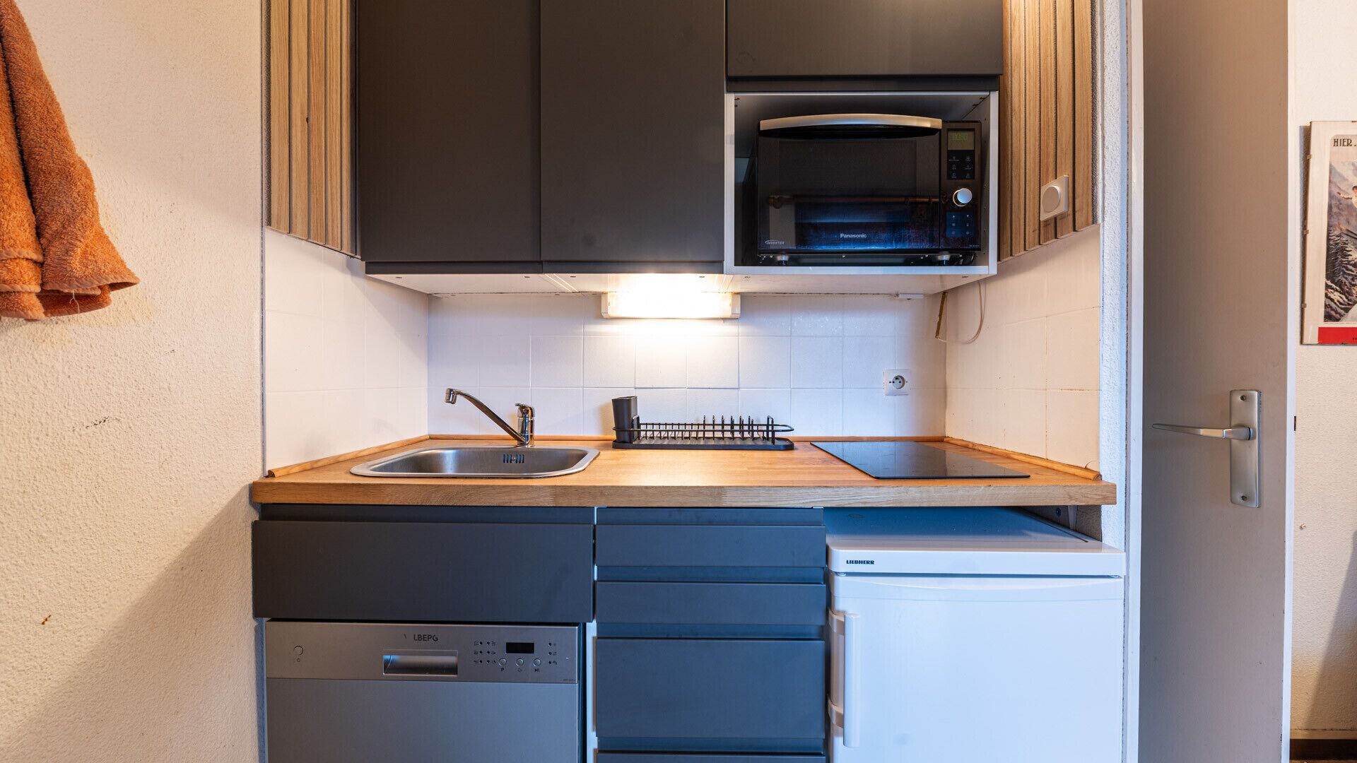 A compact kitchen with a sink, a microwave, a dishwasher, and a small refrigerator.