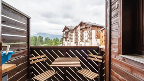 A wooden balcony with a view of a multi-story building and mountains in the background. - Lovely 4 pers studio at the foot of the pistes (Morillon)