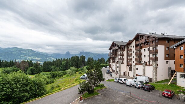 A multi-story hotel with balconies, a parking area, and a view of mountains. - Lovely 4 pers studio at the foot of the pistes (Morillon)