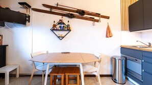 A kitchen with a wooden table, chairs, a hanging ski rack, and a shelf with bottles. - Lovely 4 pers studio at the foot of the pistes (Morillon)