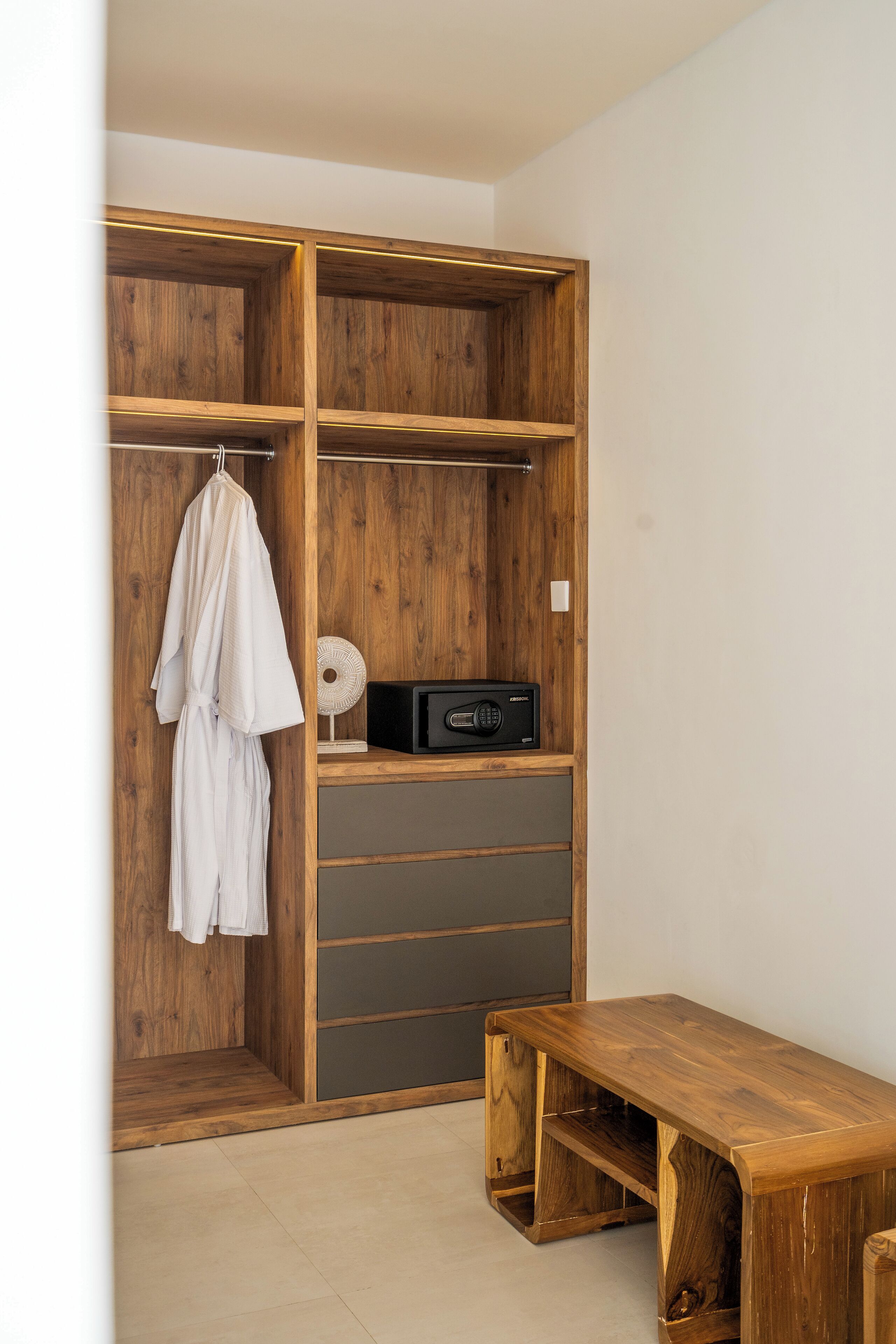 A wooden wardrobe with multiple shelves, a hanging robe, and a small table with a radio.