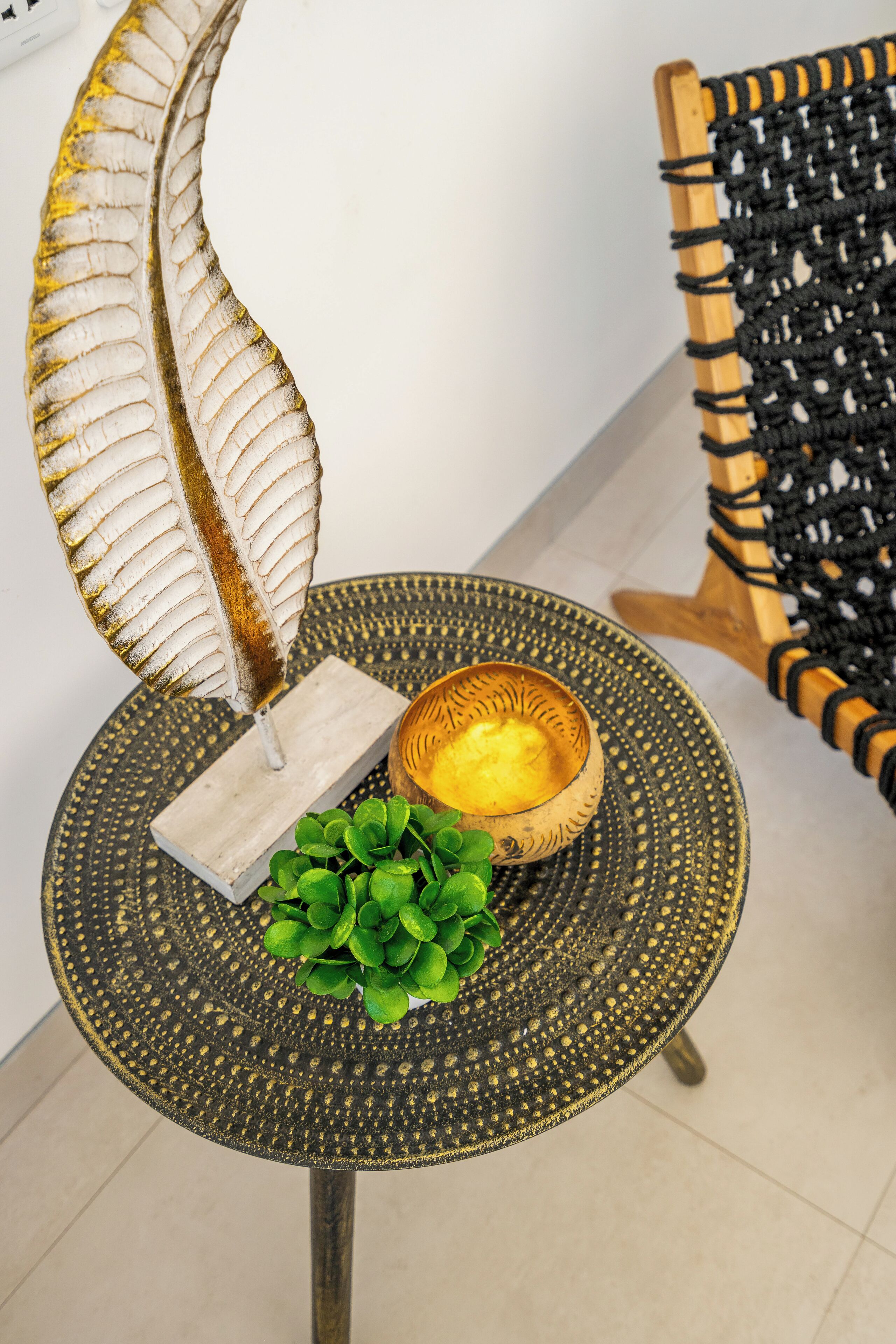 Una mesa redonda con superficie texturizada, una hoja decorativa, un pequeño bloque de madera y una planta verde.