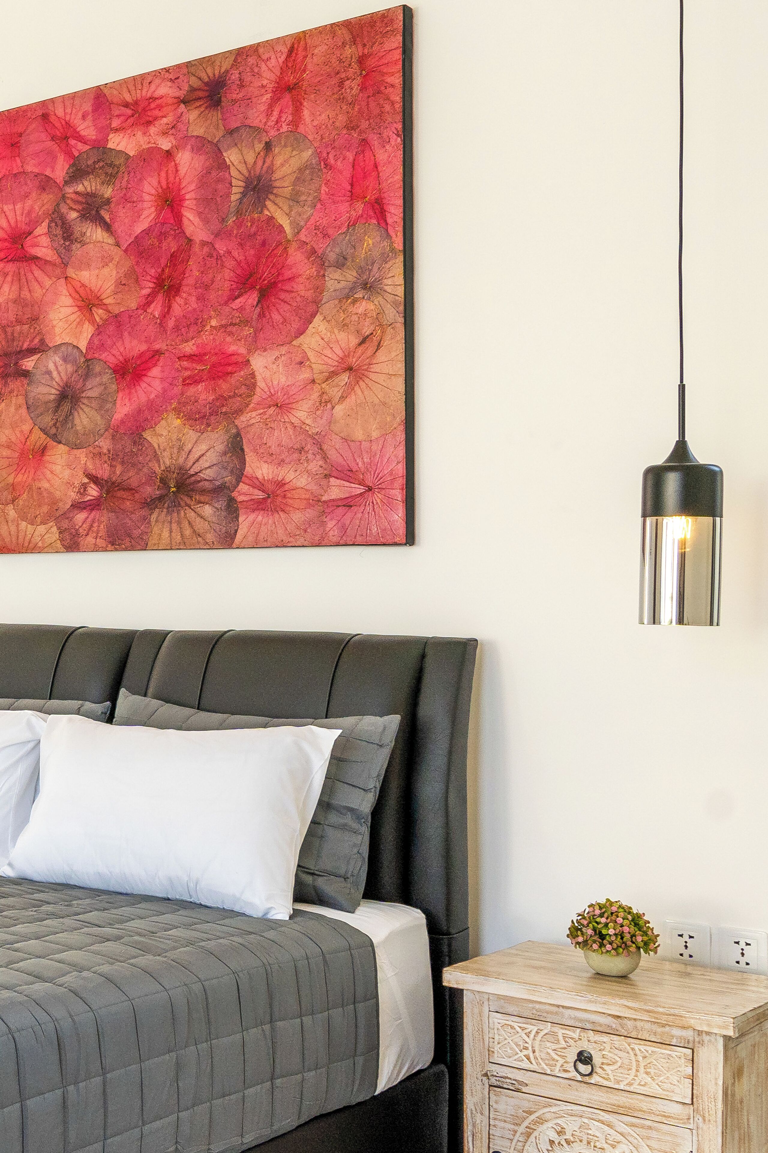 A bedroom with a bed, a nightstand, a wall-mounted lamp, and a floral artwork.