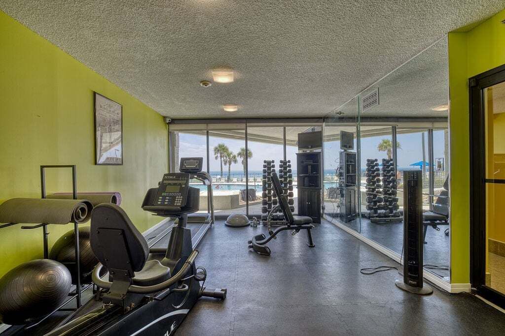 Une salle de sport équipée de matériel d’exercice, d’un tapis de course, de poids et offrant une vue sur l’océan grâce à de grandes fenêtres.