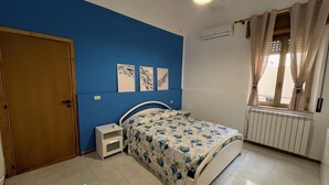 Un dormitorio con cama, mesita de noche, puerta y ventana con cortinas.