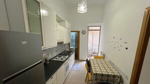 Cocina compacta con refrigerador, estufa y pileta, que da a un pequeño comedor con mesa y sillas.