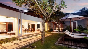 Un espace extérieur bien éclairé, comprenant une terrasse, des chaises longues et un petit arbre.