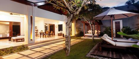 A well-lit outdoor area with a patio, lounge chairs, and a small tree.