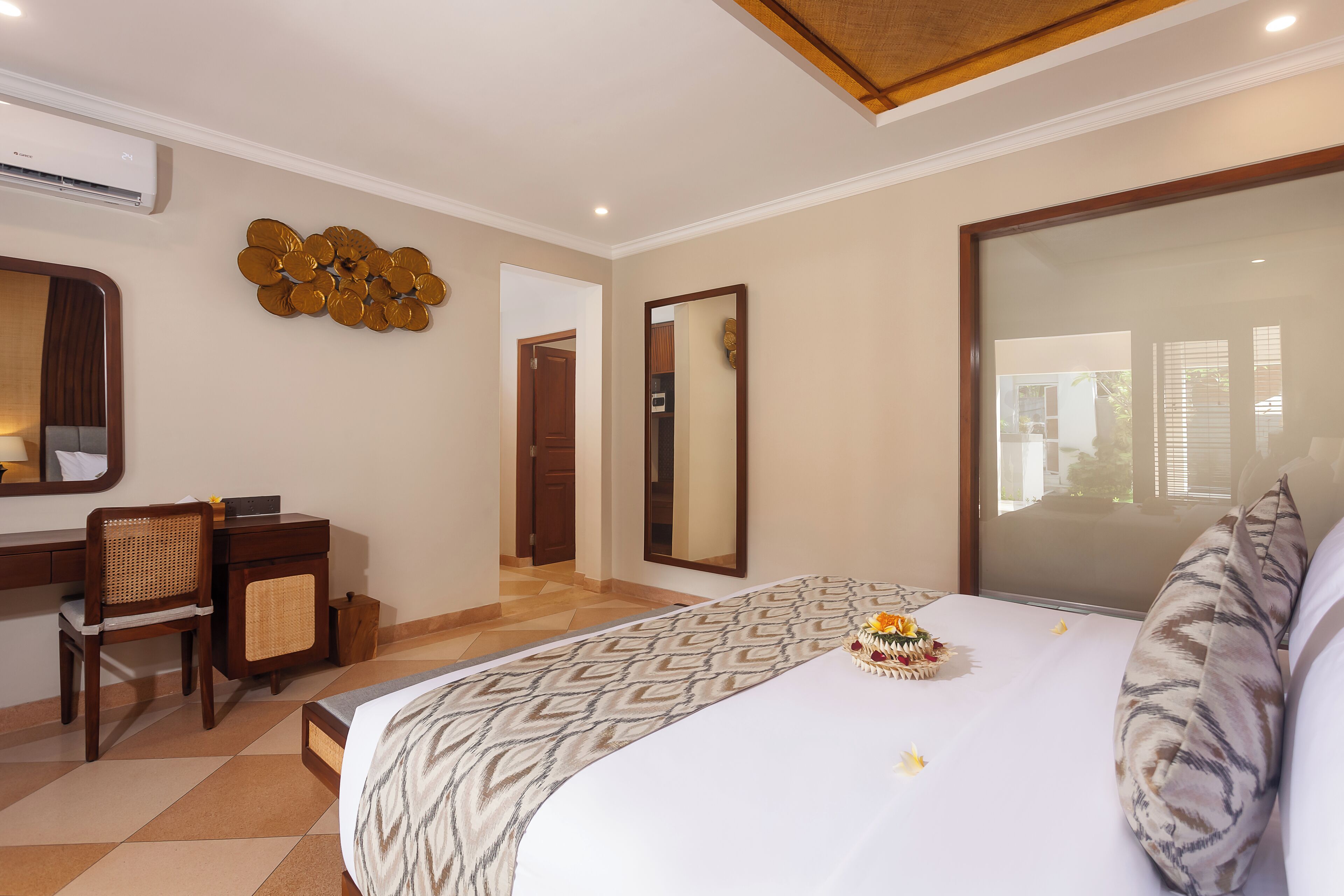 A hotel room with a bed, a desk, a chair, a large mirror, and a decorative wall piece.