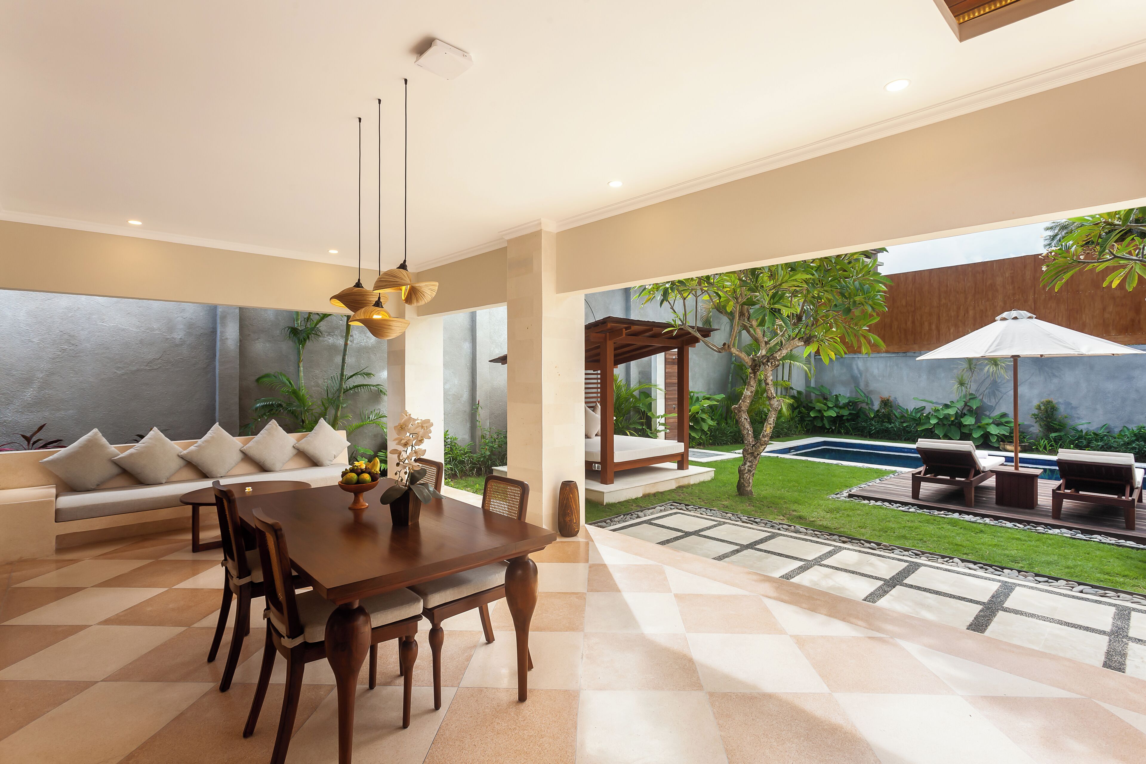 A modern dining area with a wooden table and chairs, a bench with cushions, and a view of a backyard with a pool and outdoor seating.