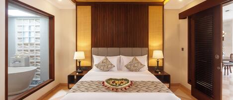 A hotel room with a large bed, two bedside tables with lamps, a mirror, and a view of a bathroom with a bathtub.