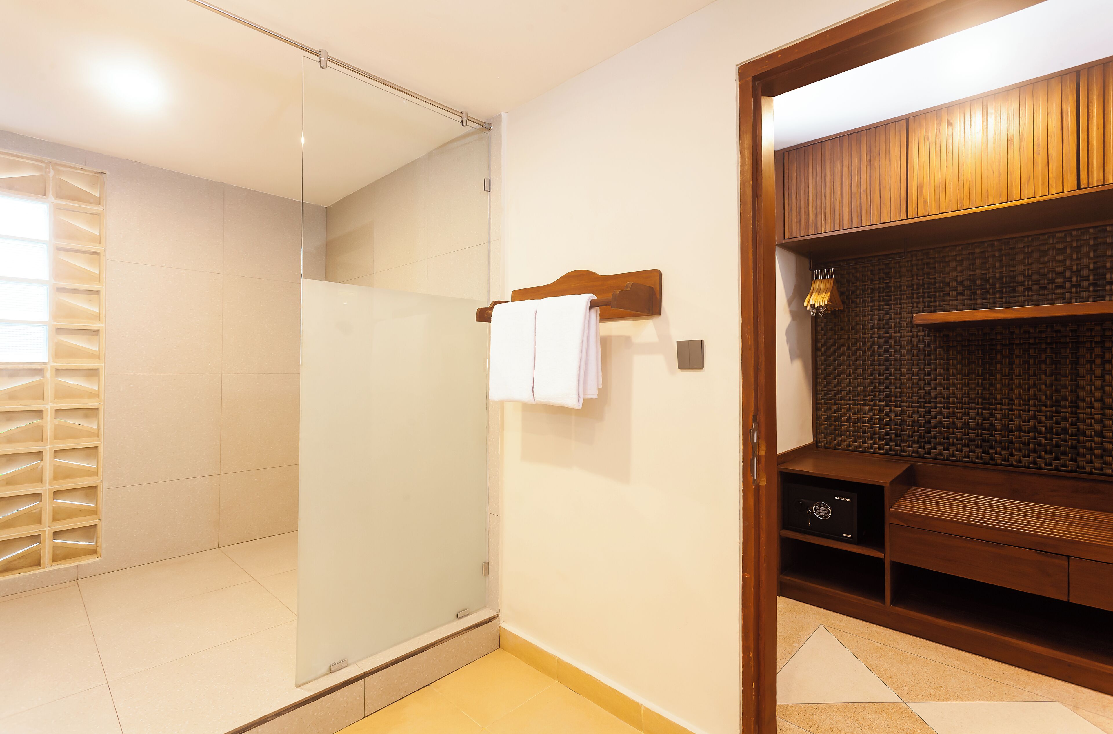 A modern bathroom with a glass shower enclosure, a wooden vanity with a towel rack, and a tiled floor.