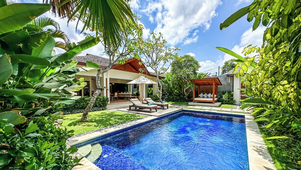 Une piscine entourée d’une végétation luxuriante, une terrasse en bois et un espace salon abrité.