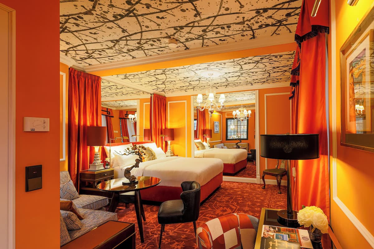 A hotel room with two beds, a sitting area with a sofa and armchair, a small table, and a mirror.