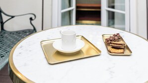 A table with a cup and a dessert on a tray, a wall-mounted light, and a door leading to a room with a chandelier.