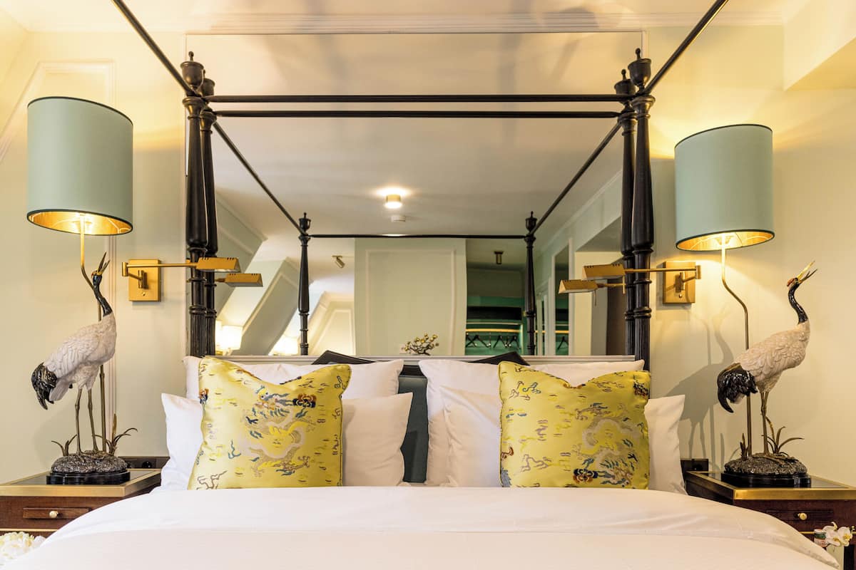 A bedroom with a four-poster bed, decorative lamps, and wall-mounted sconces.