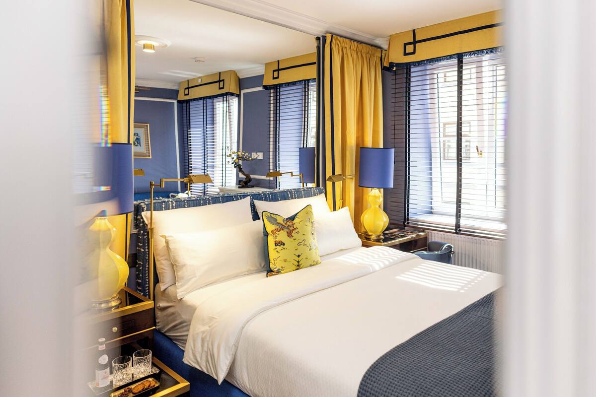 A hotel room with a large bed, two bedside tables, a nightstand, and a window with blinds.