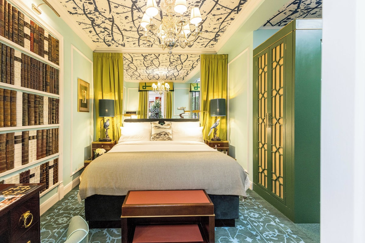 A bedroom with a large bed, a bookshelf, a chandelier, and a green door.