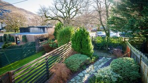 Un jardin avec un chemin de pierres, une clôture en bois et divers arbustes.