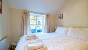 Une chambre d’hôtel avec un grand lit, du linge de lit blanc, une fenêtre avec des rideaux, une petite poubelle et un tableau encadré au mur.