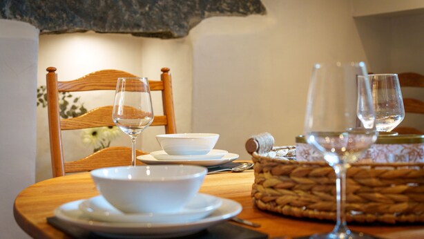 Une table à manger avec des bols, des assiettes et des verres à vin blancs, un panier en osier et une chaise en bois.