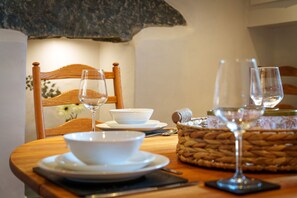 Una mesa con fuentes y platos blancos, copas de vino, una cesta tejida y una silla de madera.