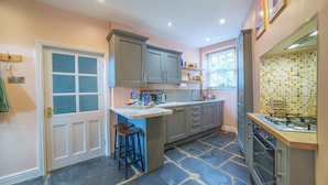 Une cuisine avec un sol en pierre, des meubles de couleur grise, une cuisinière encastrée et une fenêtre donnant sur un beau paysage.
