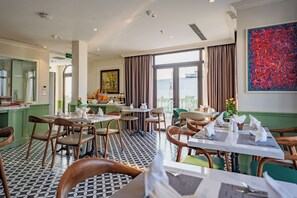 Un restaurante con piso a cuadros en blanco y negro, paredes verdes y sillas de madera. Las mesas están dispuestas con manteles y servilletas blancos.