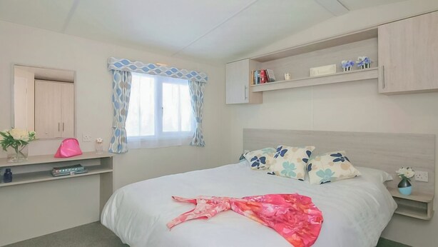 A bedroom with a bed, a window with curtains, a bedside table, a shelf with books, and a wardrobe.