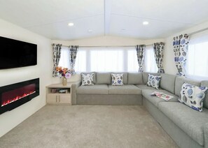 A living room with a sofa, a flat-screen TV, a fireplace, and patterned curtains.