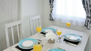 A dining table set with plates, glasses, and cutlery, with a window and curtains in the background.