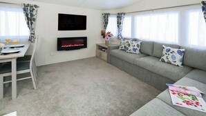 A modern living room with a flat-screen TV, a fireplace, a sofa with patterned cushions, a dining table with chairs, and a window with curtains.