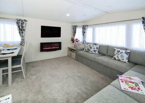 Uma sala de estar moderna com televisão de tela plana, lareira, sofá com almofadas estampadas, mesa de jantar com cadeiras e janela com cortinas.